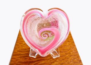 A glass heart with pink and white swirls inside of it.