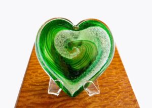 A green heart shaped glass dish on top of a wooden table.